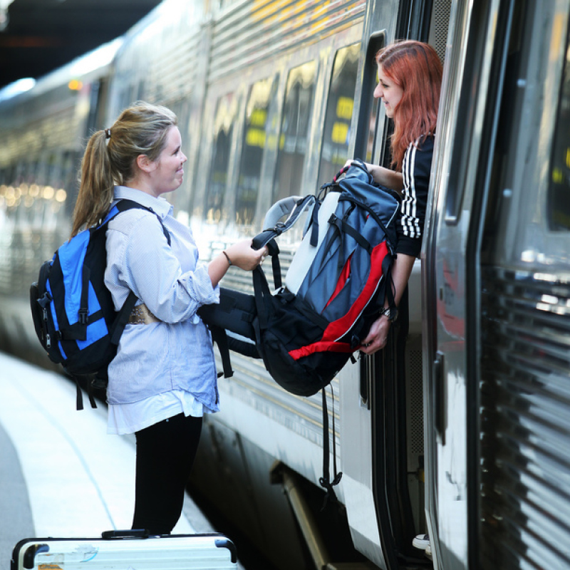 A woman passing a backpack to a friend on the door of a train at a railway station